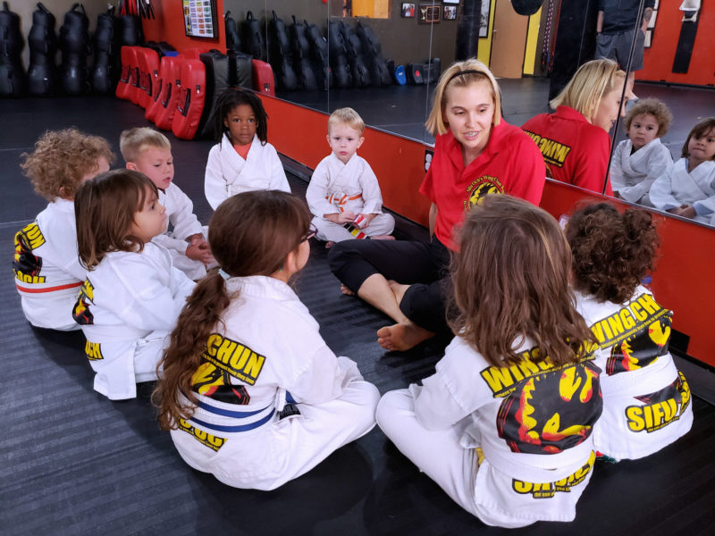kids in martial arts uniform sitting around martial arts instructor