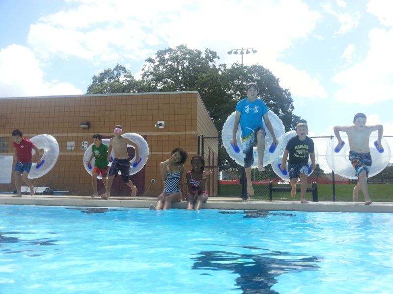 kids at summer camp jumping into pool with inner tubes