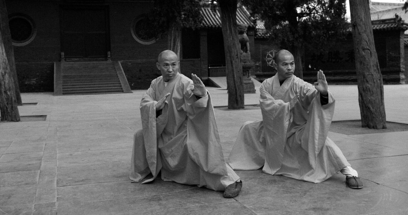 shaolin monks in front of a temple in a low kung fu pose
